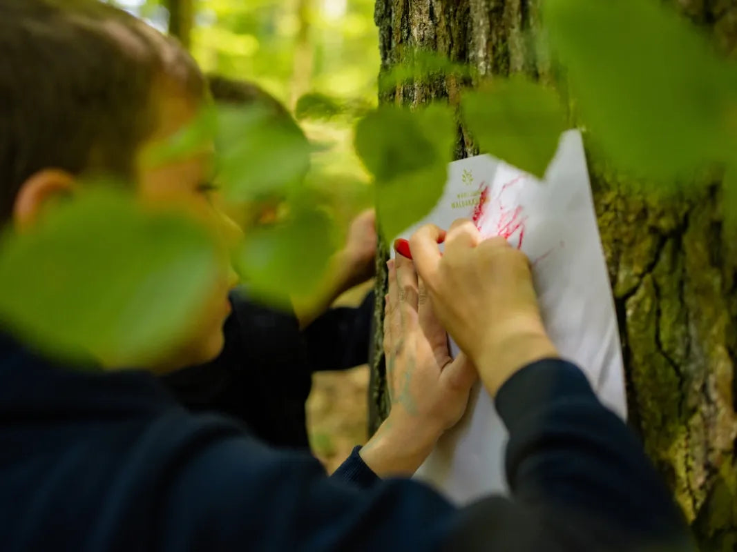 Ein Kind reibt sich in einem grünen Wald mit Rinde ein - ideal für eine Eifelwanderung mit Kindern bei Wohllebens Waldakademie, wo junge Entdecker gemeinsam die Wunder der Natur entdecken.