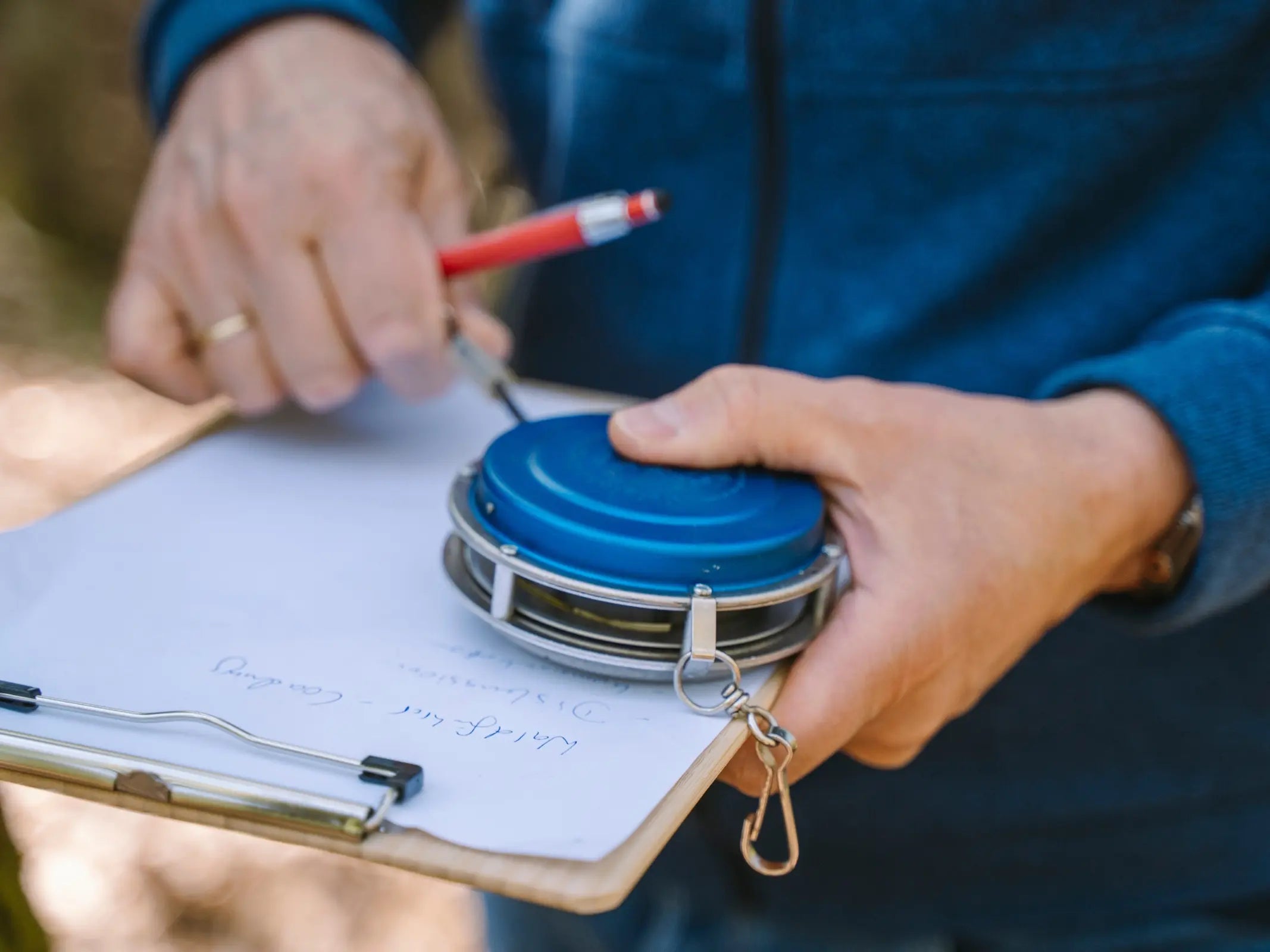 Person mit Klemmbrett und Metallmaßband, die mit einem roten Stift im Freien schreibt - ideal für Bildungsurlaub oder für alle, die praktisches Waldwissen von Wohllebens Waldakademie zur ökologischen Forstwirtschaft suchen.