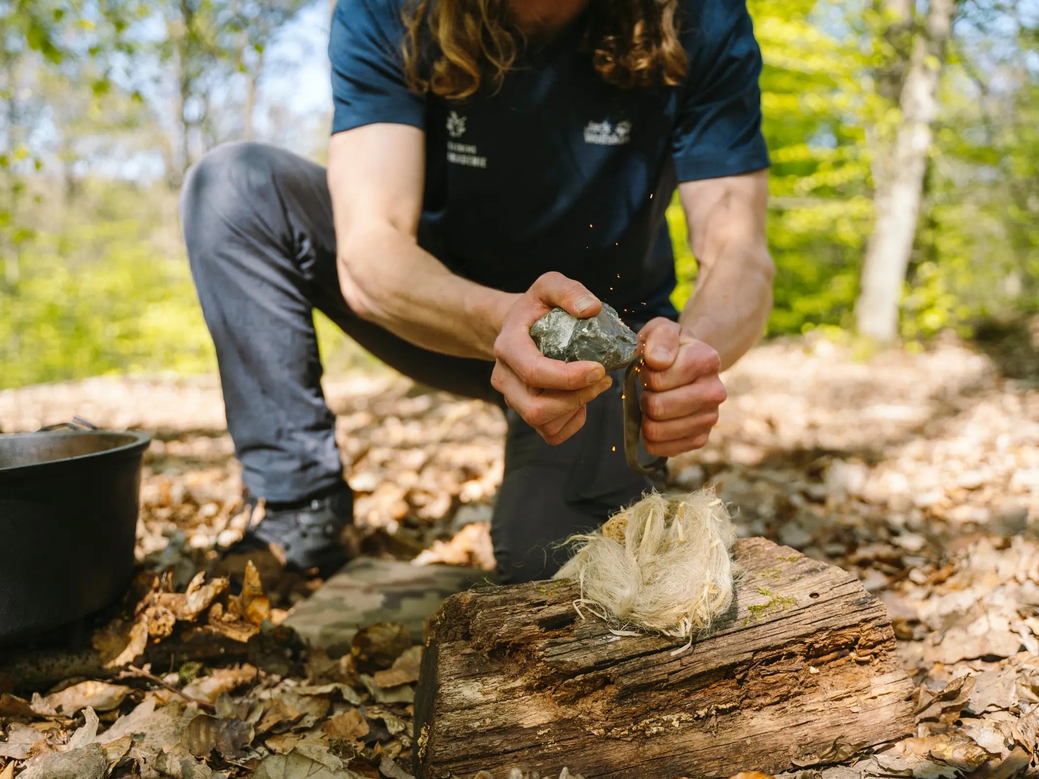 Im Wald knien, Feuerstein schlagen und mit trockenem Zunder ein Feuer auf einem Baumstamm entfachen - ein authentisches Abenteuer-Wald-Erlebnis mit Wohllebens Waldakademie.