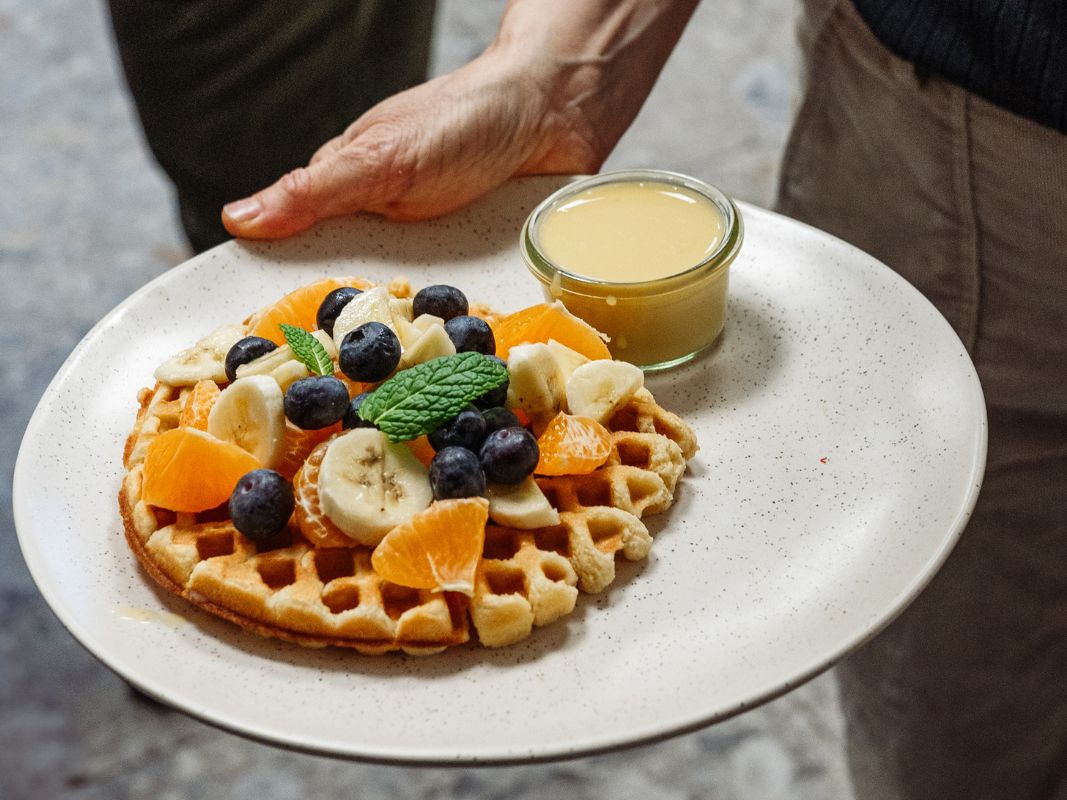 Eine Wohllebens Waldakademie-Waffel mit Banane, Blaubeeren, Orange und Minze, serviert mit Sauce - ideal zum Genießen beim Alumni-Treffen oder nach einem Waldführer-Waldpädagogik-Ausflug.
