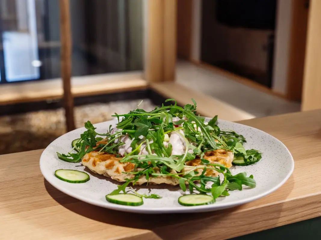 Ein Wohllebens Waldakademie Teller mit Waffeln mit Rucola, Sahne und Gurke auf einer Holztheke - ideal für ein gemütliches Waffel-Event oder als Inspiration für Weihnachtsfeier Ideen.