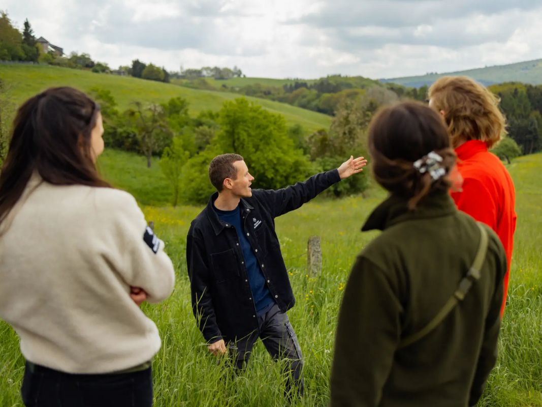 Menschen reden und gestikulieren in einer üppigen Landschaft, diskutieren über Umweltkrisen und den Schutz unserer Lebensgrundlagen und unterstreichen damit die Mission der Wohllebens Waldakademie.