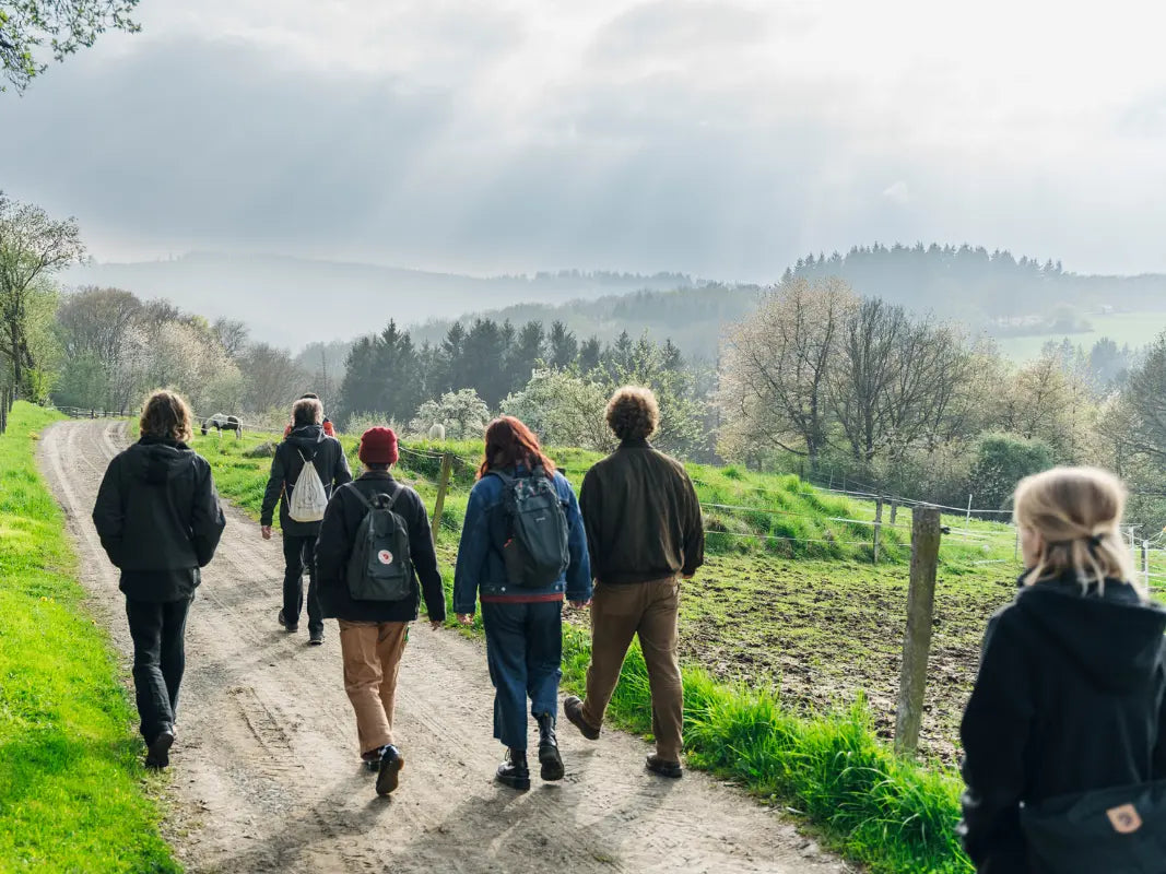 Eine Gruppe wandert auf einem ländlichen Feldweg in der Eifel, umgeben von Bäumen und Hügeln, und genießt einen Kräuterspaziergang mit Wohllebens Waldakademie, um heimische Wildpflanzen zu entdecken.